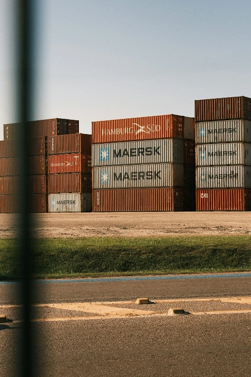 Stacks of cargo shipping containers at a port yard, representing import logistics and landed cost tracking for Oman trading companies